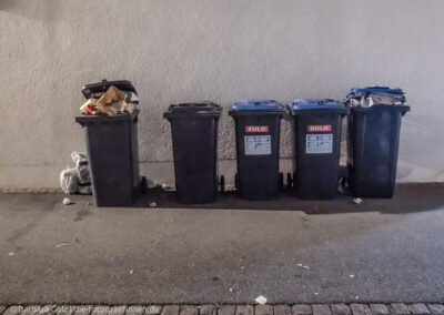 Fünf Mülltonnen nachts auf der Straße vor einer Wand