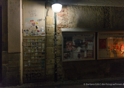 Informationstafeln an einer alten Mauer, beleuchtet durch eine Straßenlaterne