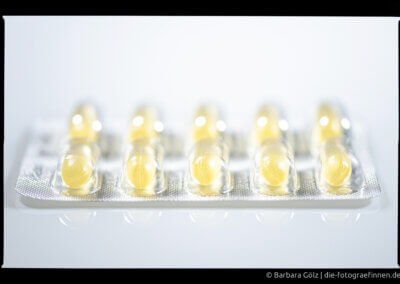 Silberfarbige Blisterpackung mit gelben Pillen vor hellem Hintergrund mit teilweiser Spiegelung