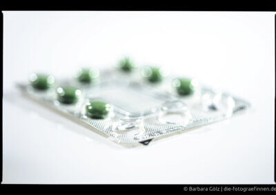 Ein silberner Blister mit grünen Pillen vor weißem Hintergrund. Drei Pillen sind schon verbraucht.