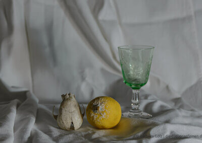 Stillleben mit einem gründen Glas mit floraler Verzierung, einer Zitrone mit Schimmelansatz und einem kleinen Tierschädel