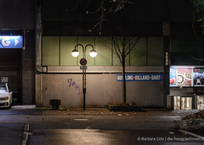 Straßenszene aus Reutlingen bei Nacht: Blick auf eine Betonwand mit einer Doppel-Laterne, rechts das Schild "Bowling – Billard – Dart", ganz rechts der Eingang in eine unterirdische Passage, beleuchtet von Werbung
